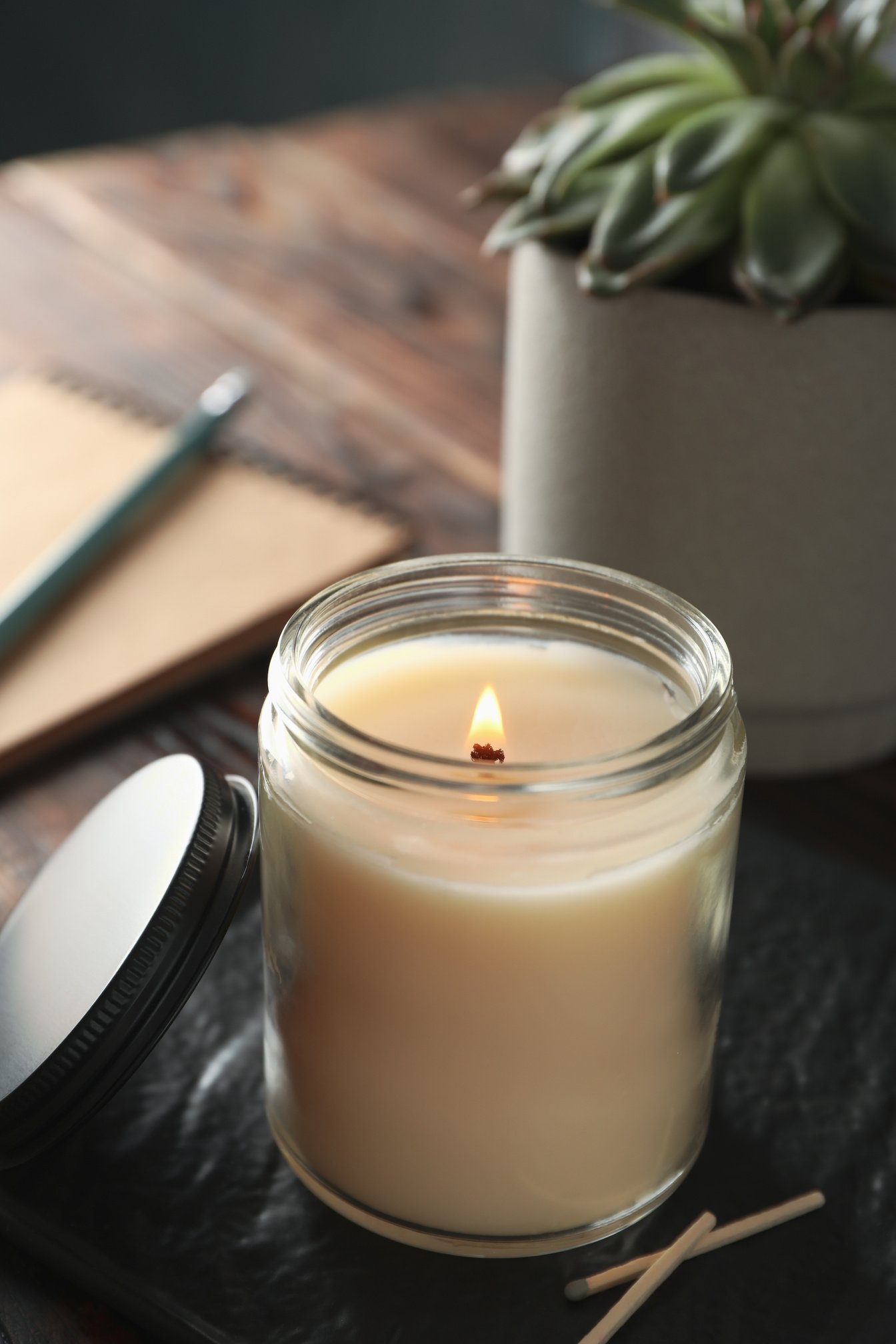 Burning Candle in Glass Jar, Succulent and Notebook on Wooden Ba